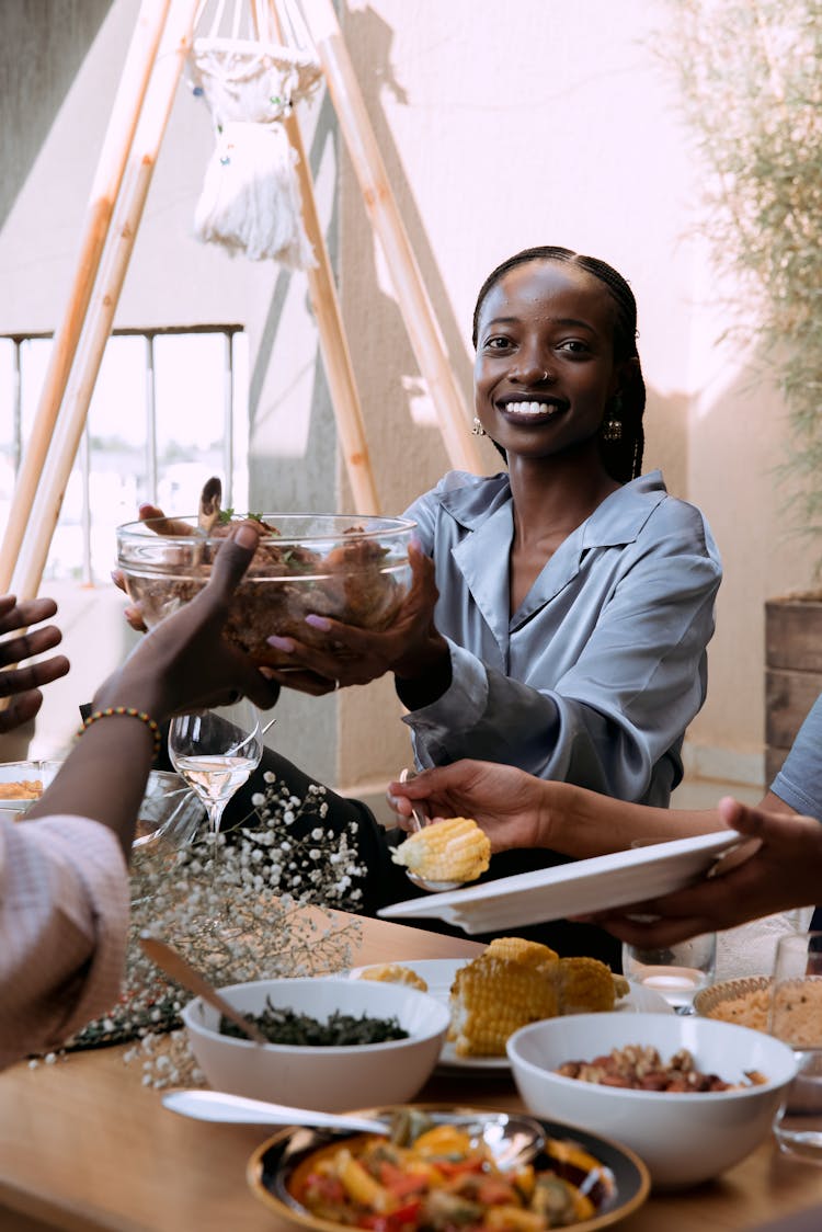 A Woman In Blue Dress Shirt Passing A Clear Glass Bowl With Food