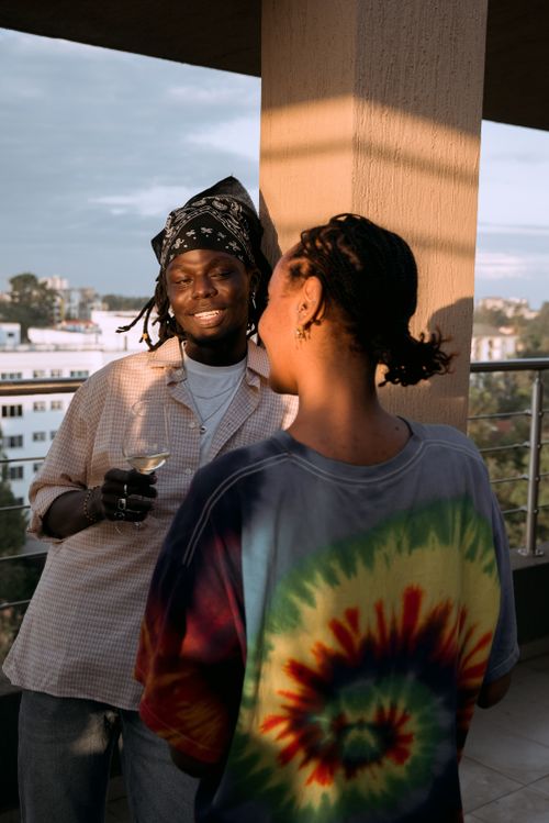 Free Two friends enjoy a casual chat on a balcony at sunset with drinks. Stock Photo