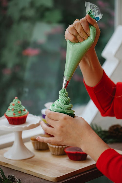 Crop woman decorating cupcake with cream