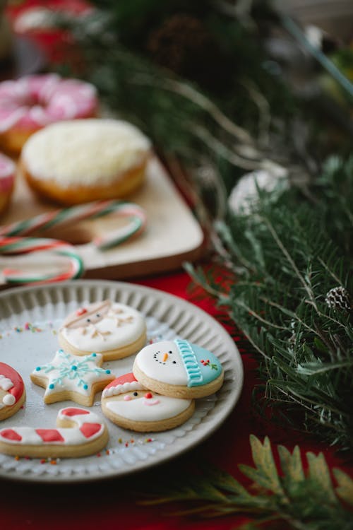 Free High angle of traditional Christmas gingerbread biscuits with colourful icing on plate on served table with desserts decorated with spruce twigs Stock Photo