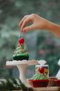 Unrecognizable woman putting red cherry on top of Christmas muffin on stand preparing for festive party