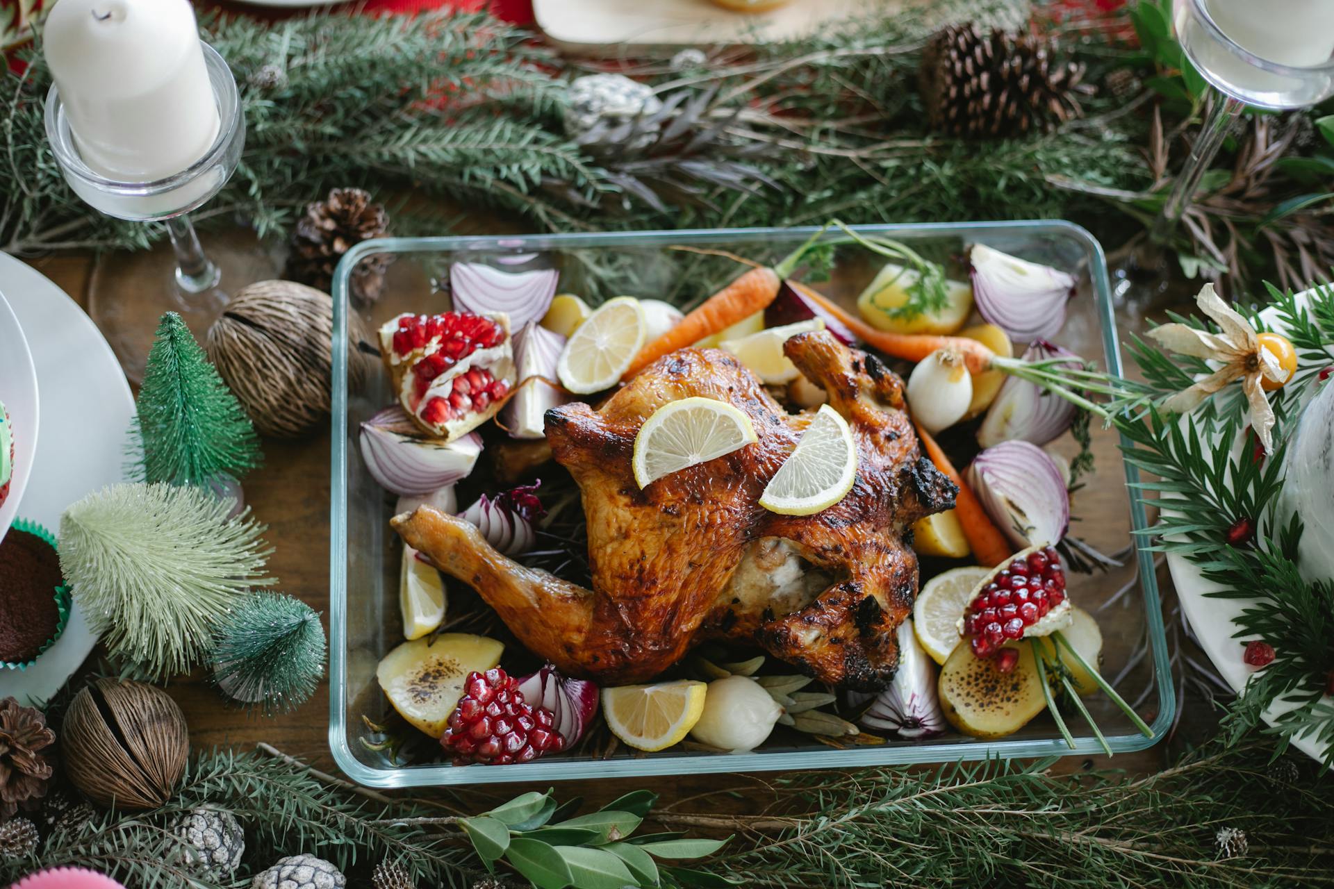 From above of traditional Christmas roasted chicken with lemons carrots and garnet in glass plate on served table decorated with coniferous twigs