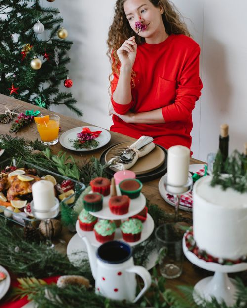 Free Dreamy woman in red sweater with flower in hand sitting at table served with dinner and desserts for Christmas party Stock Photo