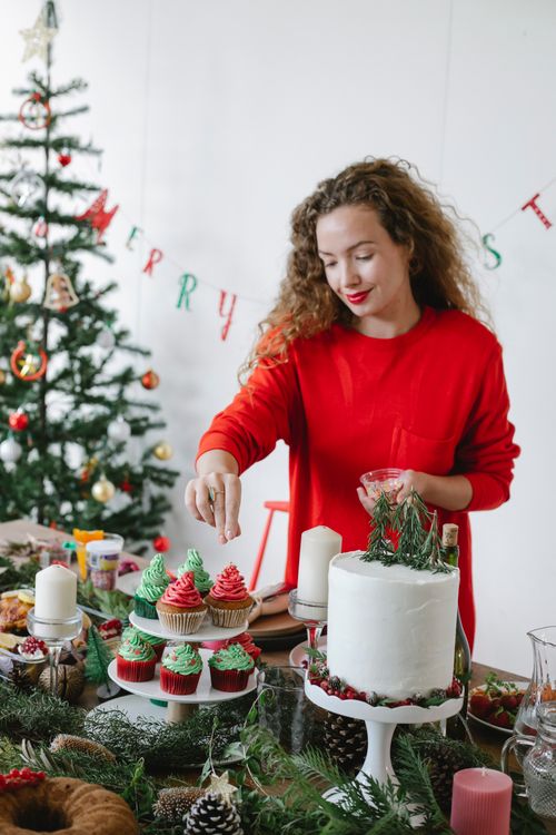 Free Smiling female cook sprinkling delicious cupcakes with buttercream on top while preparing for Christmas holiday at home Stock Photo