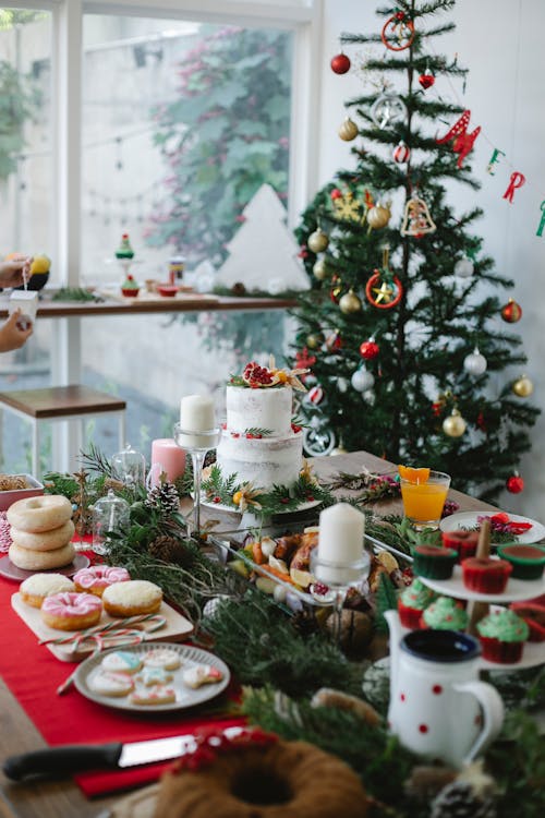 Table with assorted desserts near Christmas tree at home