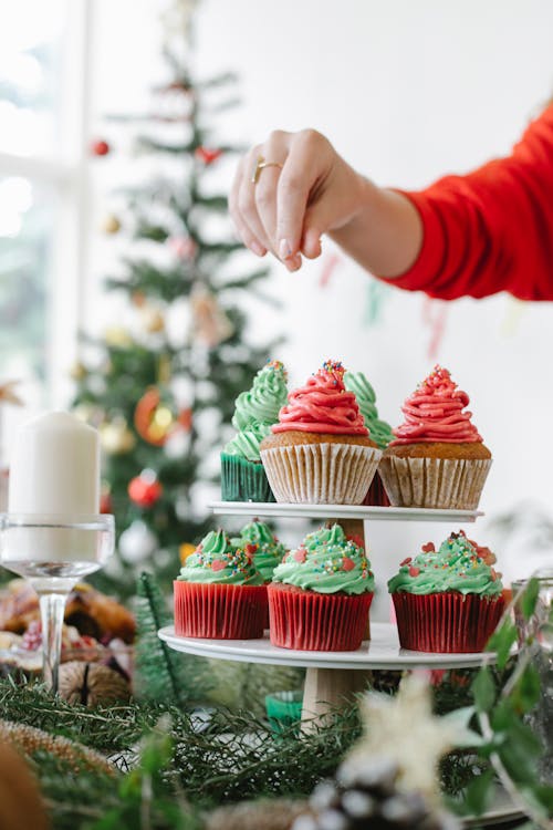 Crop anonymous female chef decorating appetizing cupcakes with buttercream on top during New Year holiday in house