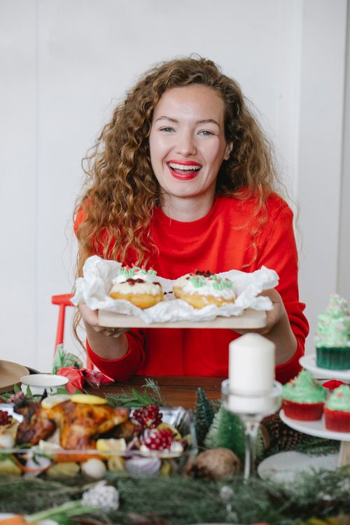 Free Sincere adult female in red wear with delicious donuts looking at camera during New Year holiday in house Stock Photo