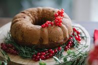 Palatable cake with ripe red berry bundle near pine sprigs on wooden tray during New Year holiday