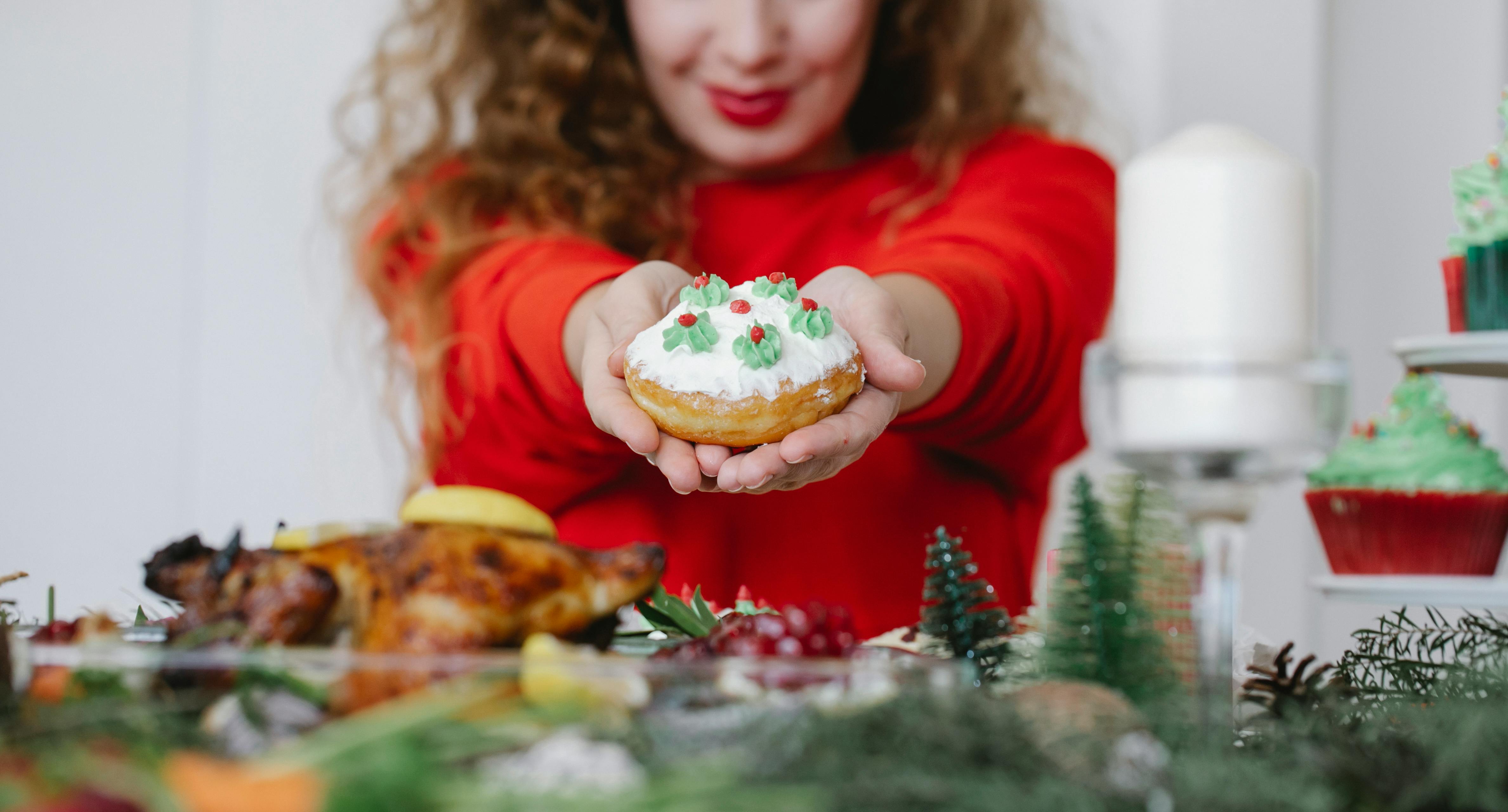 Crop anonymous smiling female with delicious doughnut decorated with buttercream on Christmas day in house