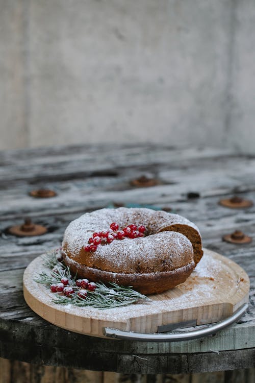 Tasty cake with ripe red berry bundle and icing sugar near fir sprigs on wooden tray during New Year holiday