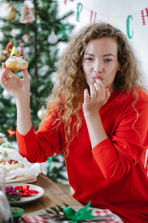 Adult female licking finger while enjoying tasty donut and looking at camera during New Year holiday at home