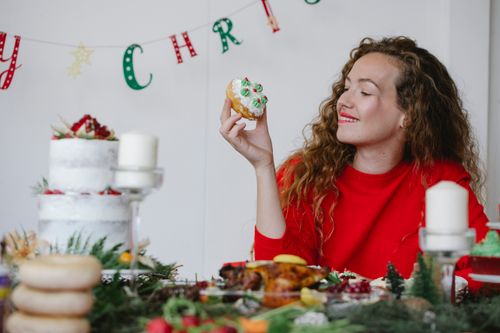 Free Smiling female with tasty donut decorated with buttercream celebrating New Year holiday at table with food at home Stock Photo