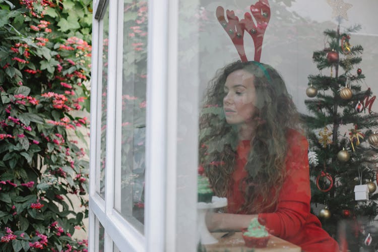 Pensive Female Sitting In Room With Christmas Decorations And Looking At Window