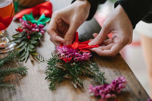 Free From above of crop faceless female florist making red bow on bouquet of lilac flowers with coniferous branches for Christmas celebration placed in daytime Stock Photo