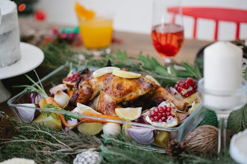 Free Roasted chicken on glass form with lemons and pomegranate and carrots on festive decorated table for Christmas celebration with cocktails and candles Stock Photo