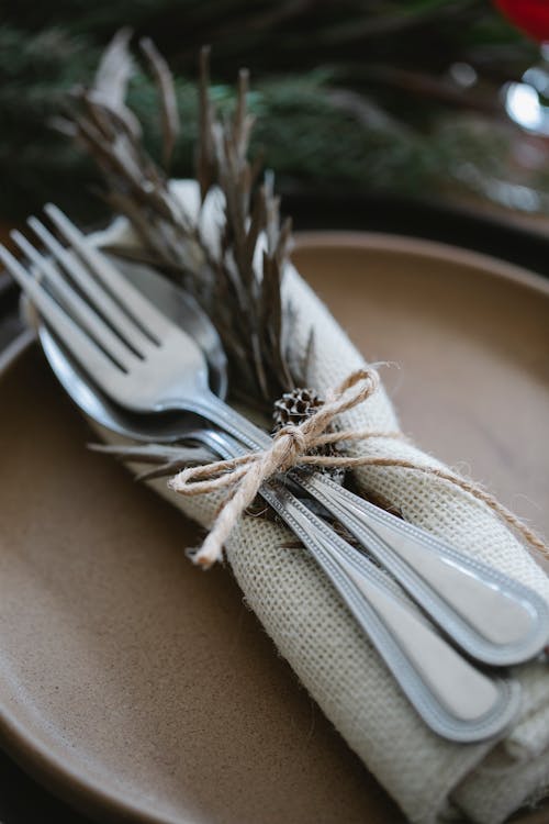From above silverware spoons and forks in linen cloth decorated with herbs on ceramic plate