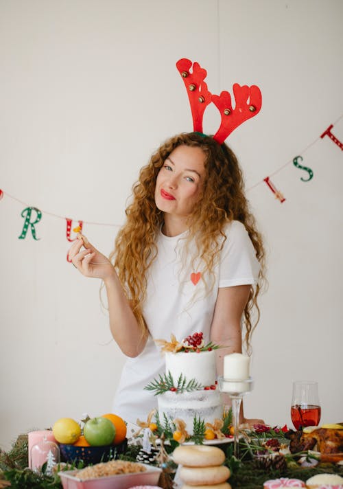 Smiling young female looking at camera while standing at table with various decorations and desserts during Christmas celebration