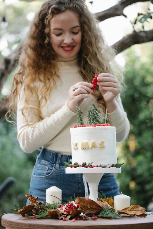 Free Young female in casual clothes decorating delicious homemade Christmas cake with berries and herbs in garden Stock Photo