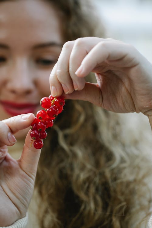 Crop female with waving hair holding twig of with red currant berries in daylight