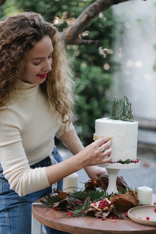 Attractive female standing at table in garden decorating cake with pomegranate seeds and pine twigs