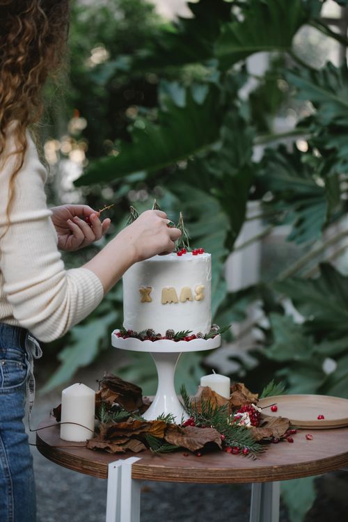 Free Side view of crop anonymous female cook decorating tasty cake with red currants and fresh rosemary sprigs under Xmas title Stock Photo