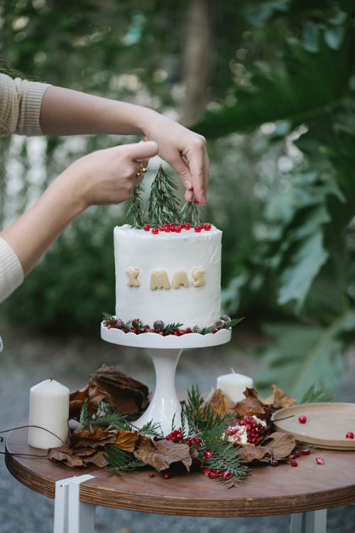 Free Crop unrecognizable female cook putting fresh rosemary sprigs on Christmas cake with decorative inscription on table Stock Photo
