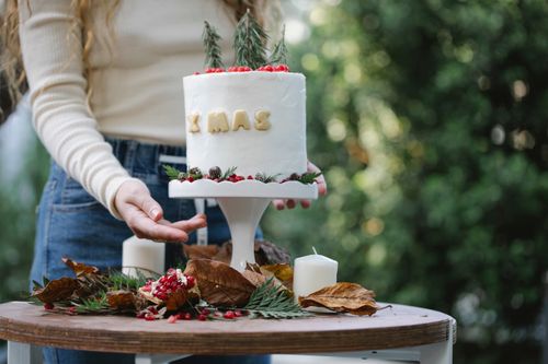 Free Crop anonymous female cook against stand with delicious cake with Xmas inscription and fresh rosemary on top Stock Photo