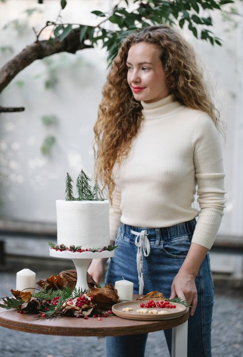 Free Adult dreamy female chef looking away at table with yummy New Year cake with fresh rosemary sprigs on top Stock Photo