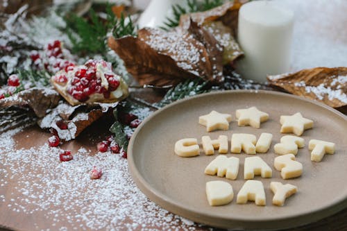 Sugar paste title with stars on ceramic plate near pomegranate seeds and fir tree sprigs during New Year holiday