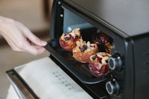 Faceless cook getting out baking tray with delicious filled baked apples of electric oven at home