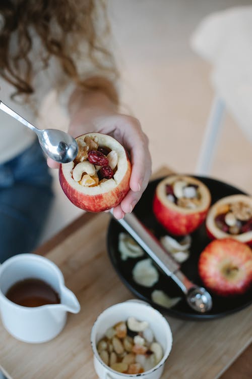 From above of crop anonymous female cook stuffing ripe apple with nuts and dried berries in house