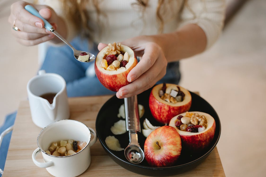 Faceless female cook with syrup in spoon and filled red apple during cooking process at home