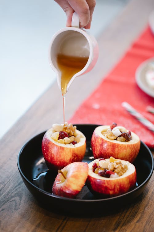 Crop anonymous cook with small jug pouring sweet syrup on filled apple in baking pan during cooking process in house