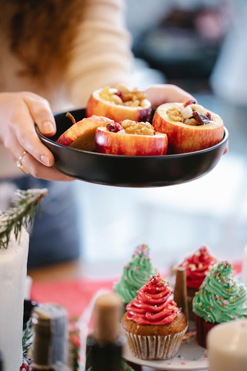 Crop chef with tasty baked apples above decorated Christmas cupcakes