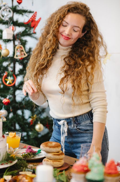 Free Smiling female cook at table with pile of delicious bagels preparing for New Year holiday in house Stock Photo