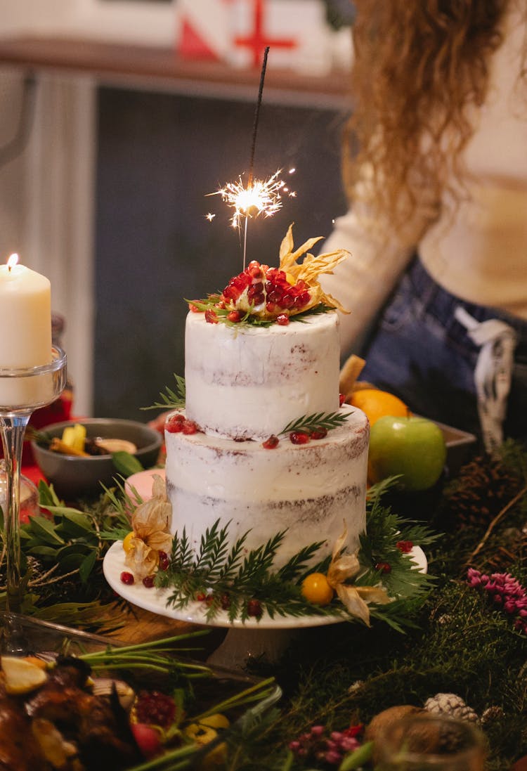 Crop Woman Against Delicious Christmas Cake With Burning Bengal Light