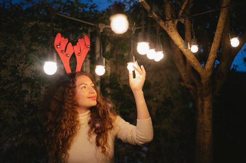Free Pondering woman touching shiny garland during Christmas holiday outdoors Stock Photo