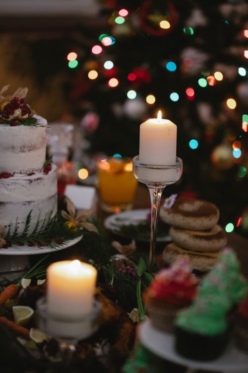 Free Flaming wax candles on table with assorted desserts against shiny garland during New Year holiday in house Stock Photo