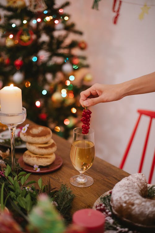 Crop anonymous person with bundle of fresh red berries above glass of alcoholic drink celebrating New Year holiday at home