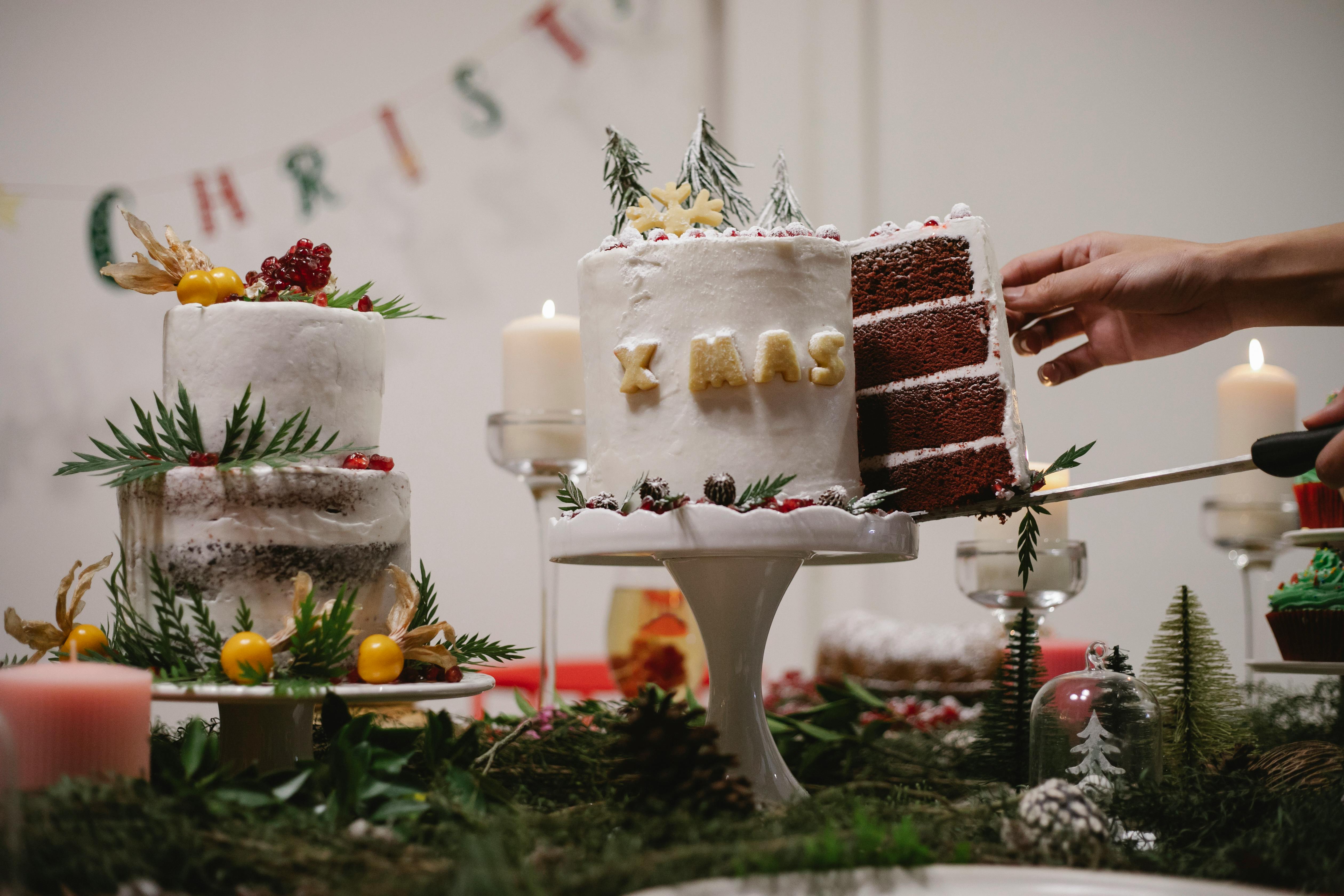 Crop anonymous cook demonstrating piece of tasty chocolate cake with Xmas inscription and rosemary decor in house