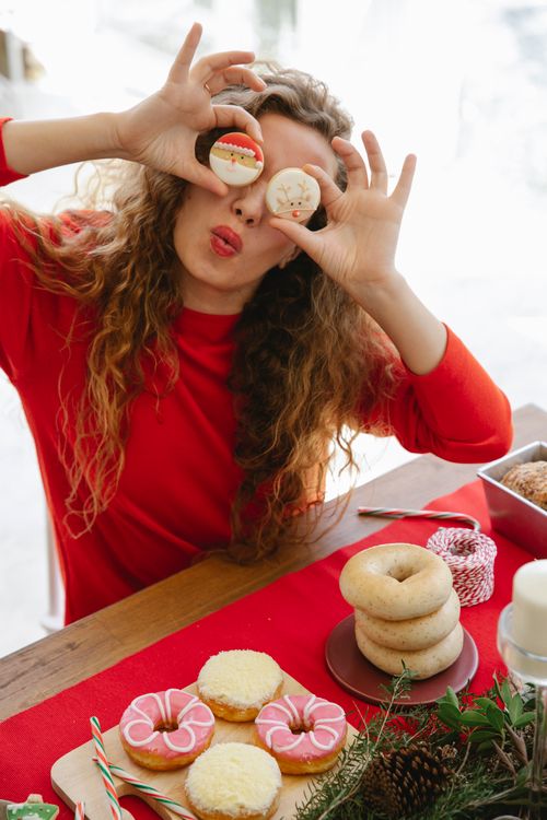 Free Female with pouting lips covering eyes with tasty gingerbread biscuits at table with assorted doughnuts and bagels during New Year holiday Stock Photo