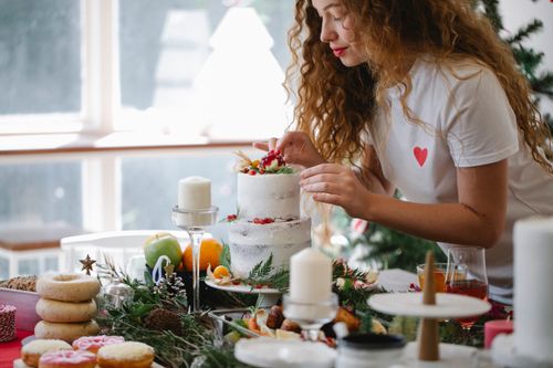 Free Crop serious female adding berries on top of two tier cake for festive dinner for New Year holiday Stock Photo