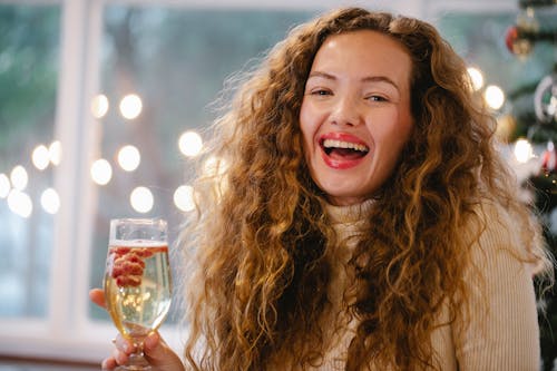 Laughing female with mouth opened with glass of sparkling champagne with red currant berries celebrating Christmas Eve