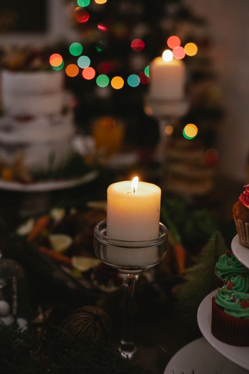 Free Festive dinner on table decorated with burning candle against fir tree with shining garland at Christmas Eve Stock Photo