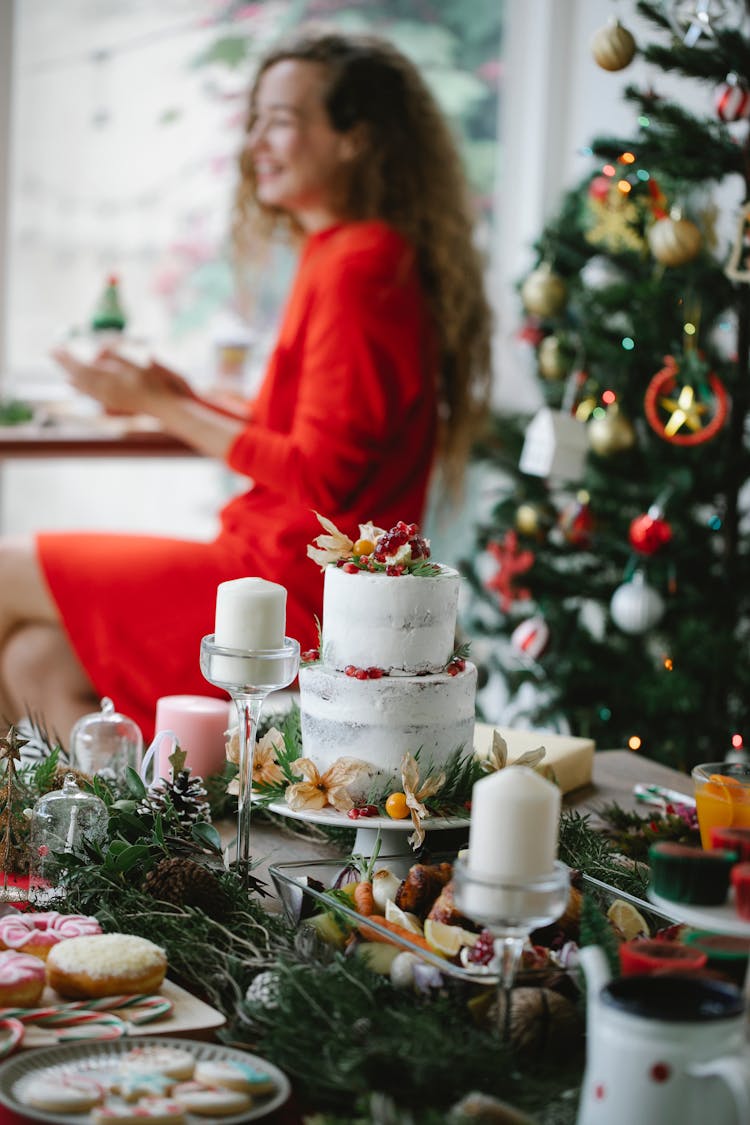 Smiling Woman Sitting Near Table With Dinner And Christmas Tree