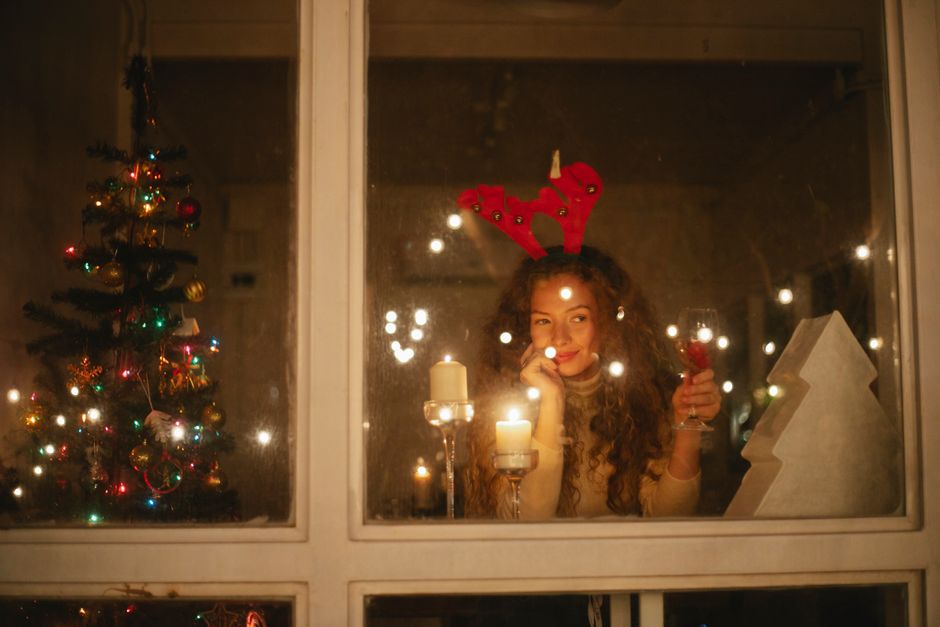 paw print tree decoration - Woman with antler headband enjoying festive evening by candlelight through a window