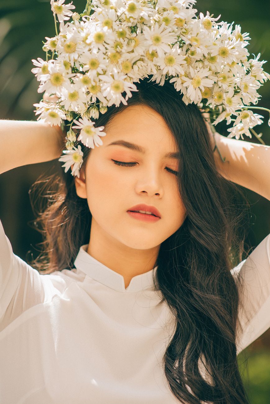 Beautiful Asian woman adorned with daisies, eyes closed, enjoying a serene moment in Vietnam outdoors.