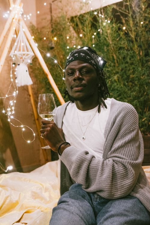 Free A relaxed man enjoying a glass of wine indoors with cozy string lights. Stock Photo