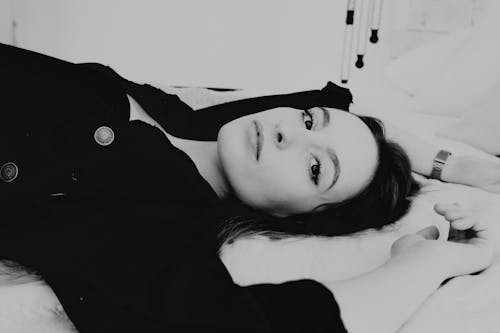 Black and white of dark haired woman looking at camera while lying in light room