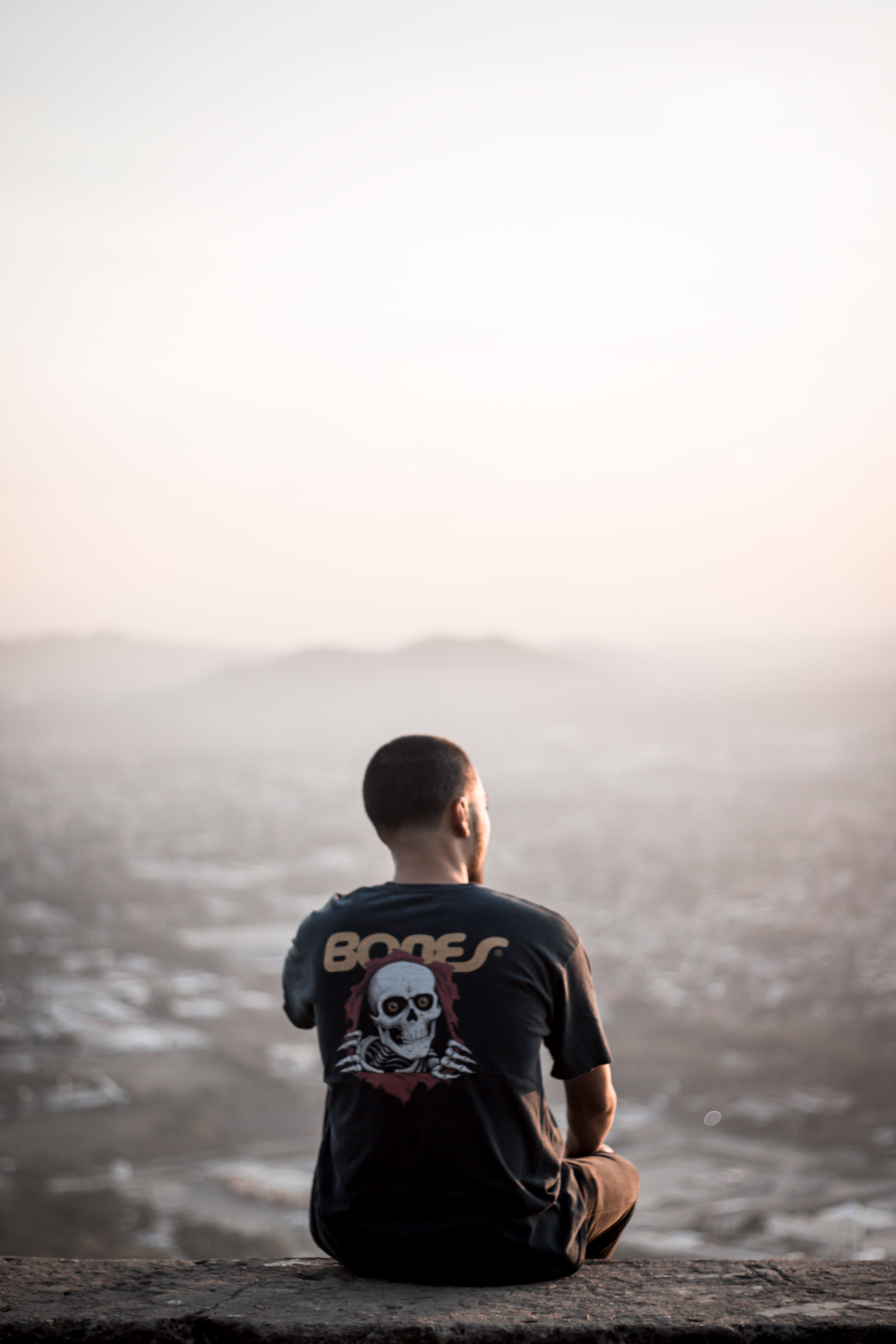 Man sitting on a ledge, overlooking San Pedro Sula at twilight, creating a reflective mood.